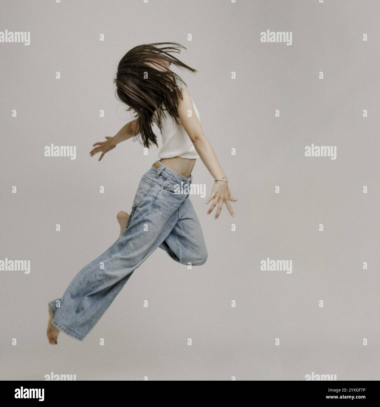 Ragazza dai capelli scuri, 10 anni, in jeans blu, salta Foto Stock
