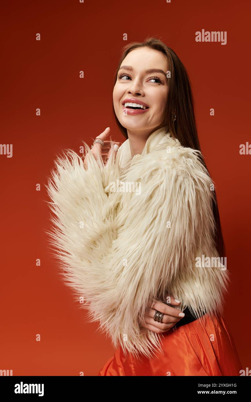 Una donna vivace posa con un sorriso brillante, indossando un elegante cappotto in pelliccia in un ambiente dai toni caldi. Foto Stock
