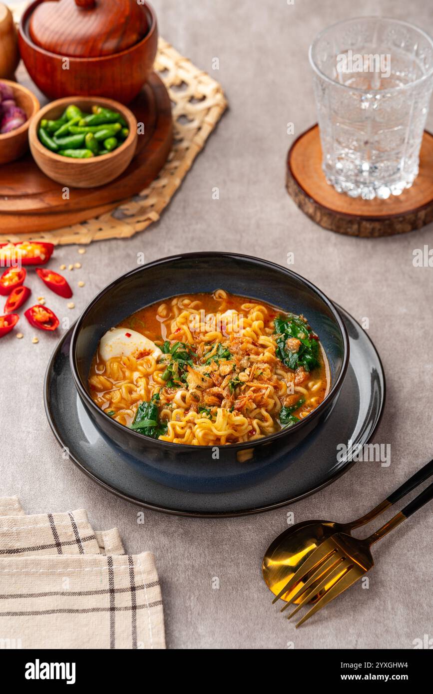 Indomie mie Kuah Telur è una zuppa indonesiana di spaghetti istantanei servita su una ciotola nera con uova sode e peperoncino. Foto Stock