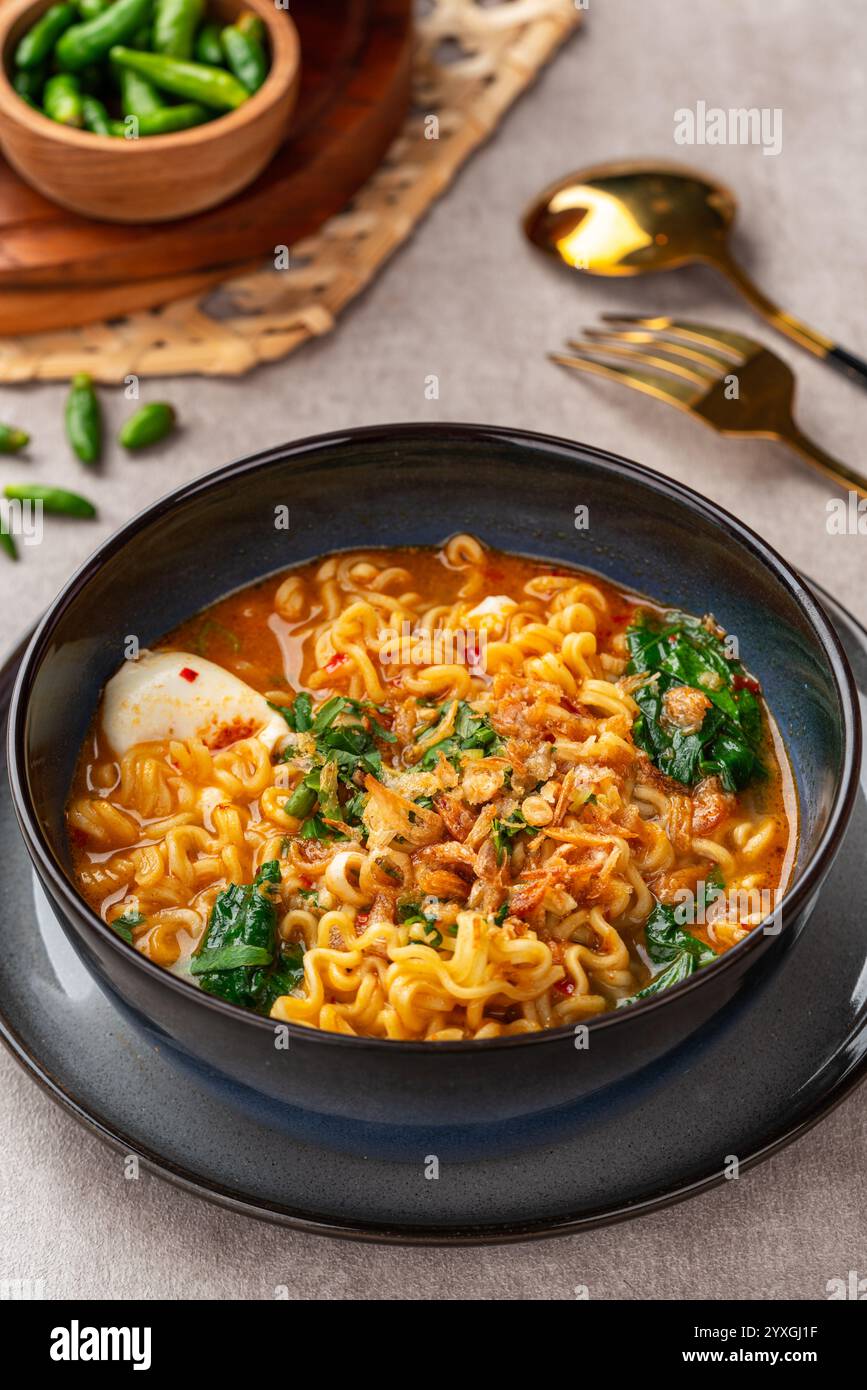 Indomie mie Kuah Telur è una zuppa indonesiana di spaghetti istantanei servita su una ciotola nera con uova sode e peperoncino. Foto Stock