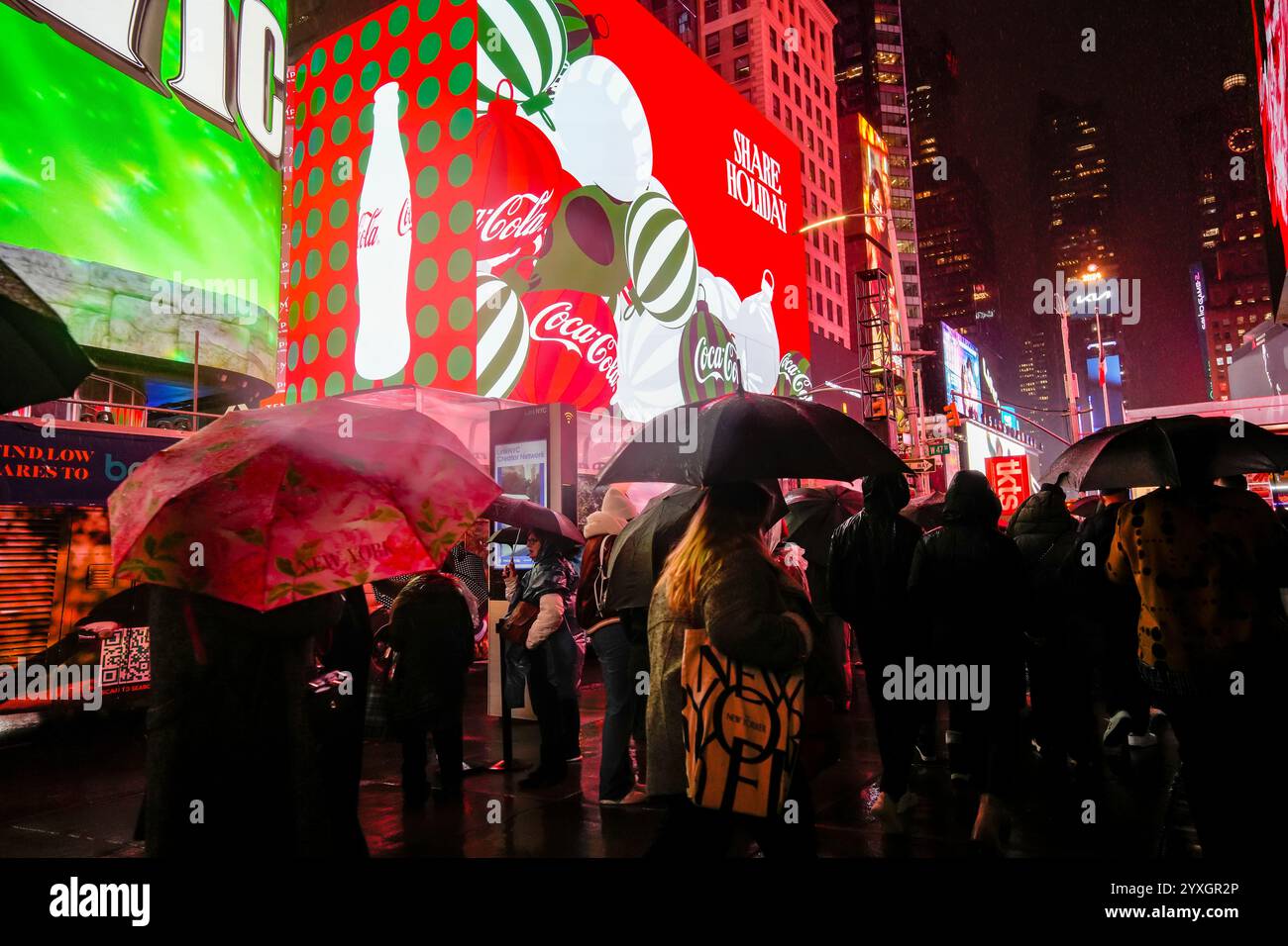 I visitatori di Times Square a New York mercoledì 11 dicembre 2024 camminano sotto la pioggia sotto i cartelloni digitali a tema natalizio che pubblicizzano Coca-Cola. (© Richard B. Levine) Foto Stock