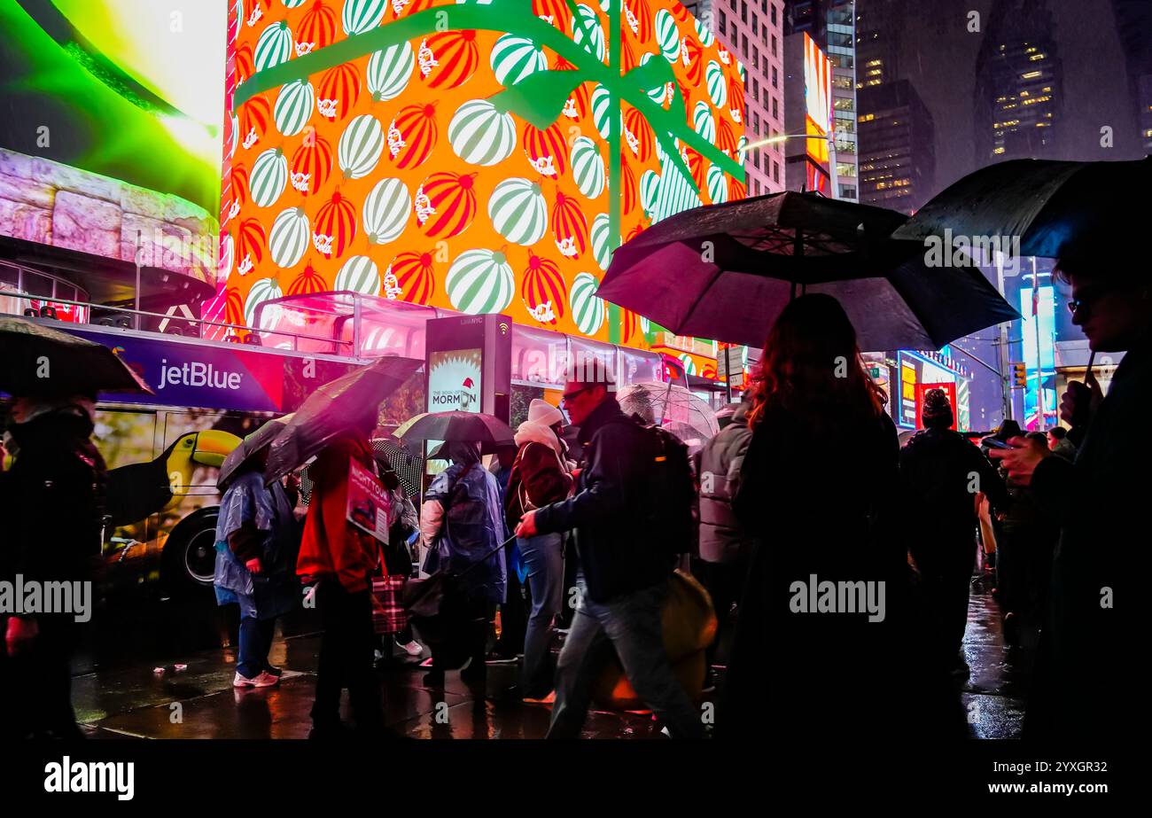 I visitatori di Times Square a New York mercoledì 11 dicembre 2024 camminano sotto la pioggia sotto i cartelloni digitali a tema natalizio che pubblicizzano Coca-Cola. (© Richard B. Levine) Foto Stock