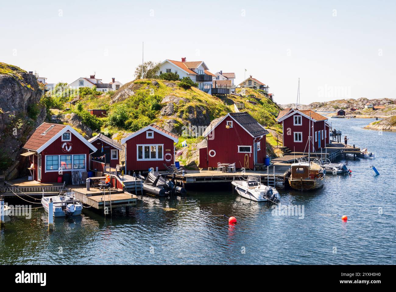 Paesaggio con tipici cottage dipinti di rosso e motoscafi ormeggiati in un molo di legno nella provincia di Bohuslän sulla costa occidentale svedese in una giornata di sole. Foto Stock