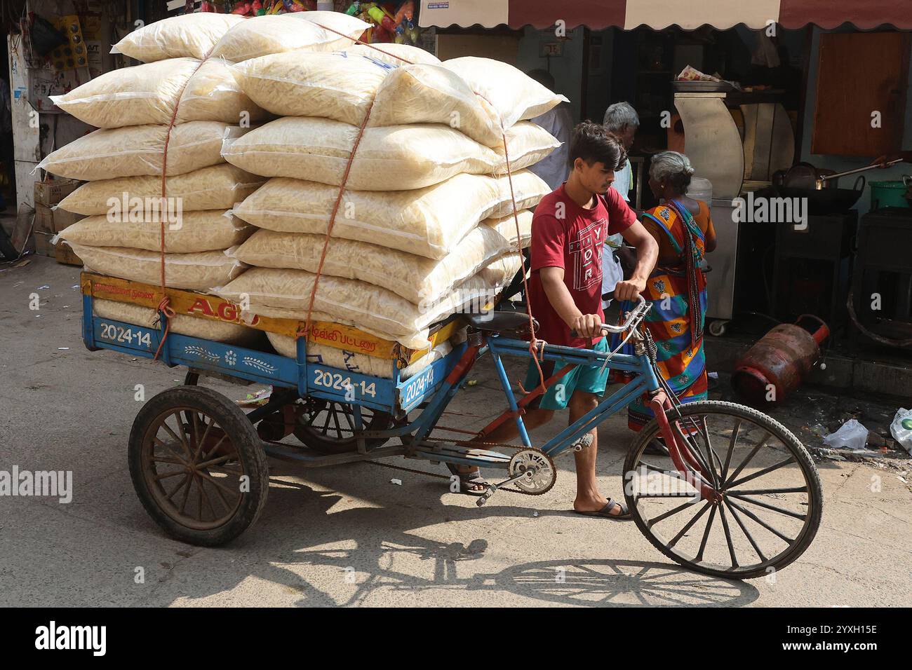 Un coolie che spinge un carrello per biciclette carico di merci nel distretto George Town di Chennai, Tamil Nadu, India Foto Stock