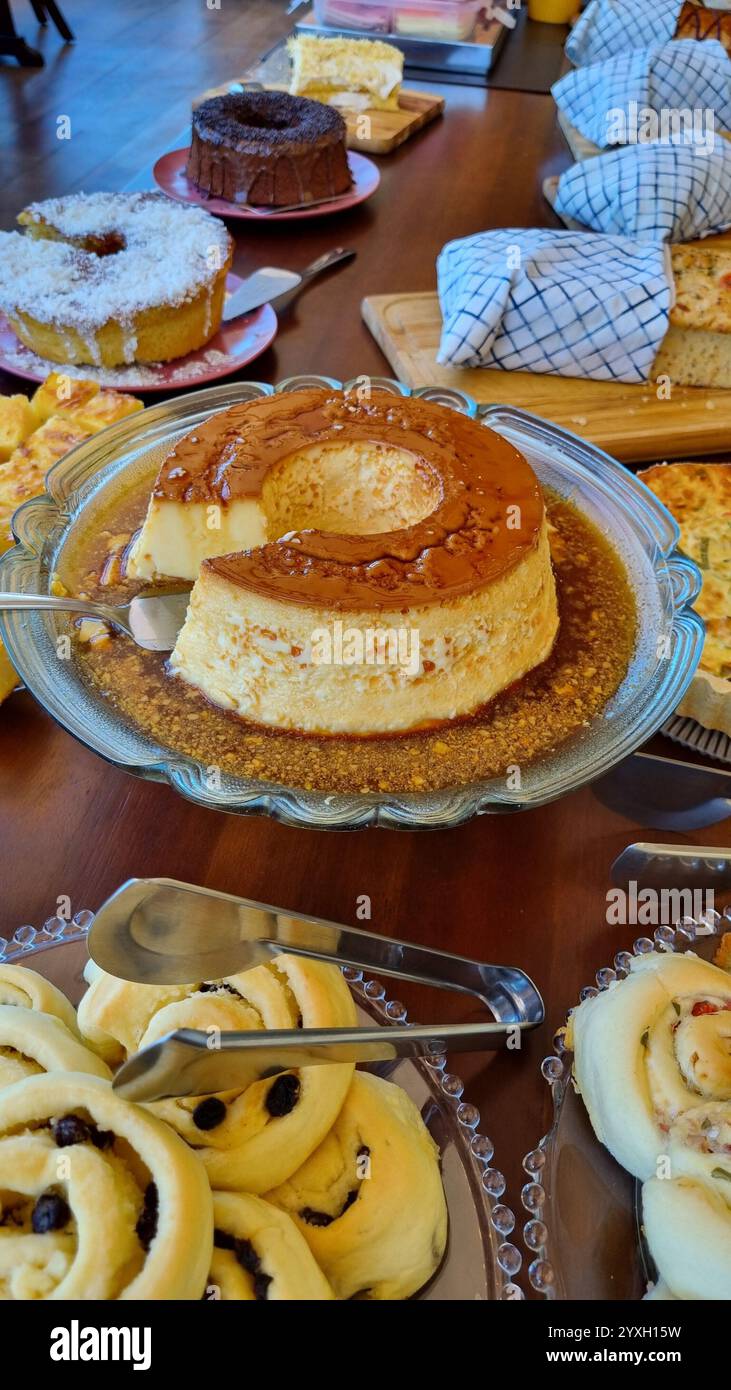 Un tavolo pieno di una varietà di dessert e prodotti da forno. Il pezzo centrale è un flan dorato con salsa al caramello su un piatto di vetro. - Immagine stock catturata con smartphone