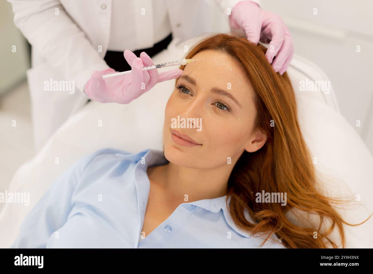 Il paziente si rilassa su un comodo letto di trattamento mentre un professionista esperto applica il filler dermico per migliorare le caratteristiche del viso in una tranquilla clinica envi Foto Stock