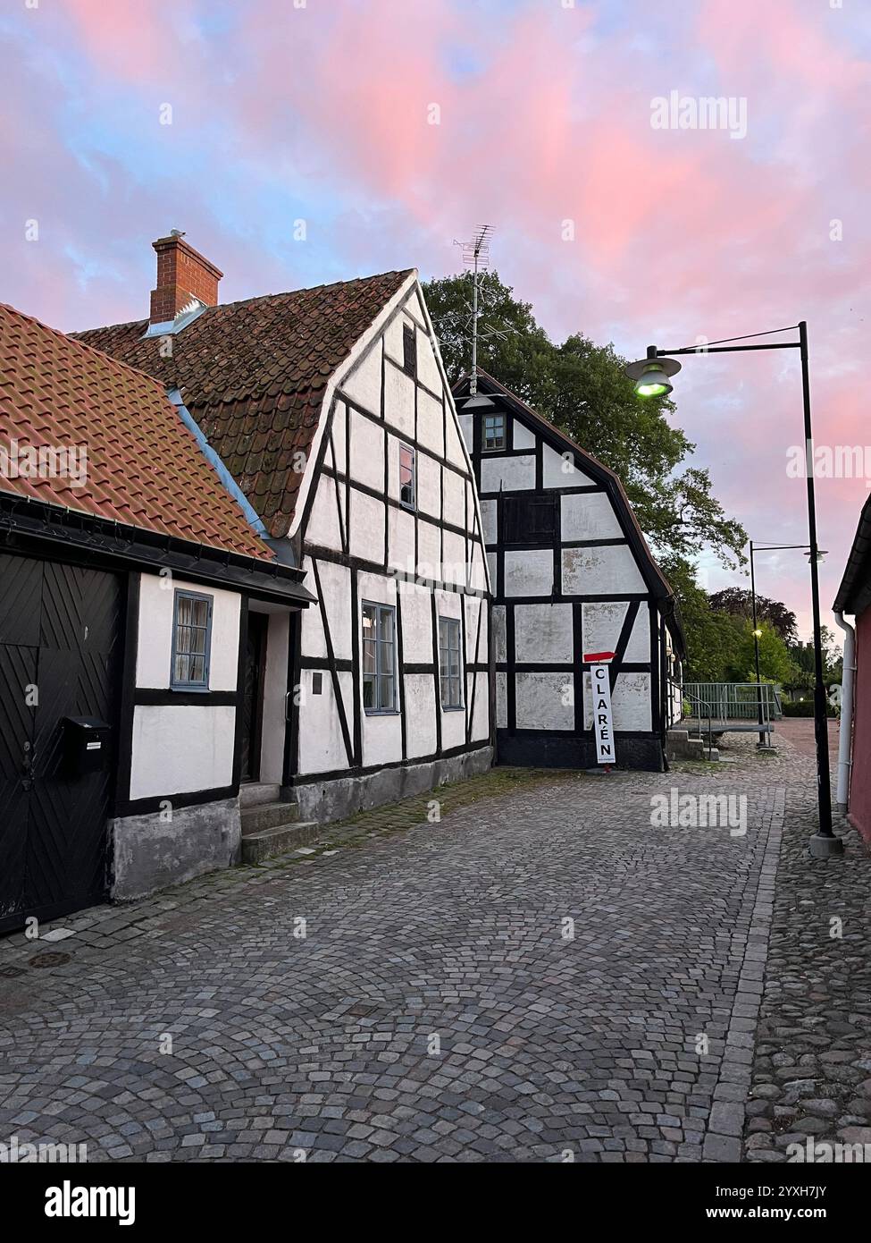 Vecchia casa bianca e marrone con tetto in mattoni rossi e pietre di ciottoli davanti e un bellissimo cielo rosa. Foto scattata a Österlen, Svezia, estate 2023 Foto Stock