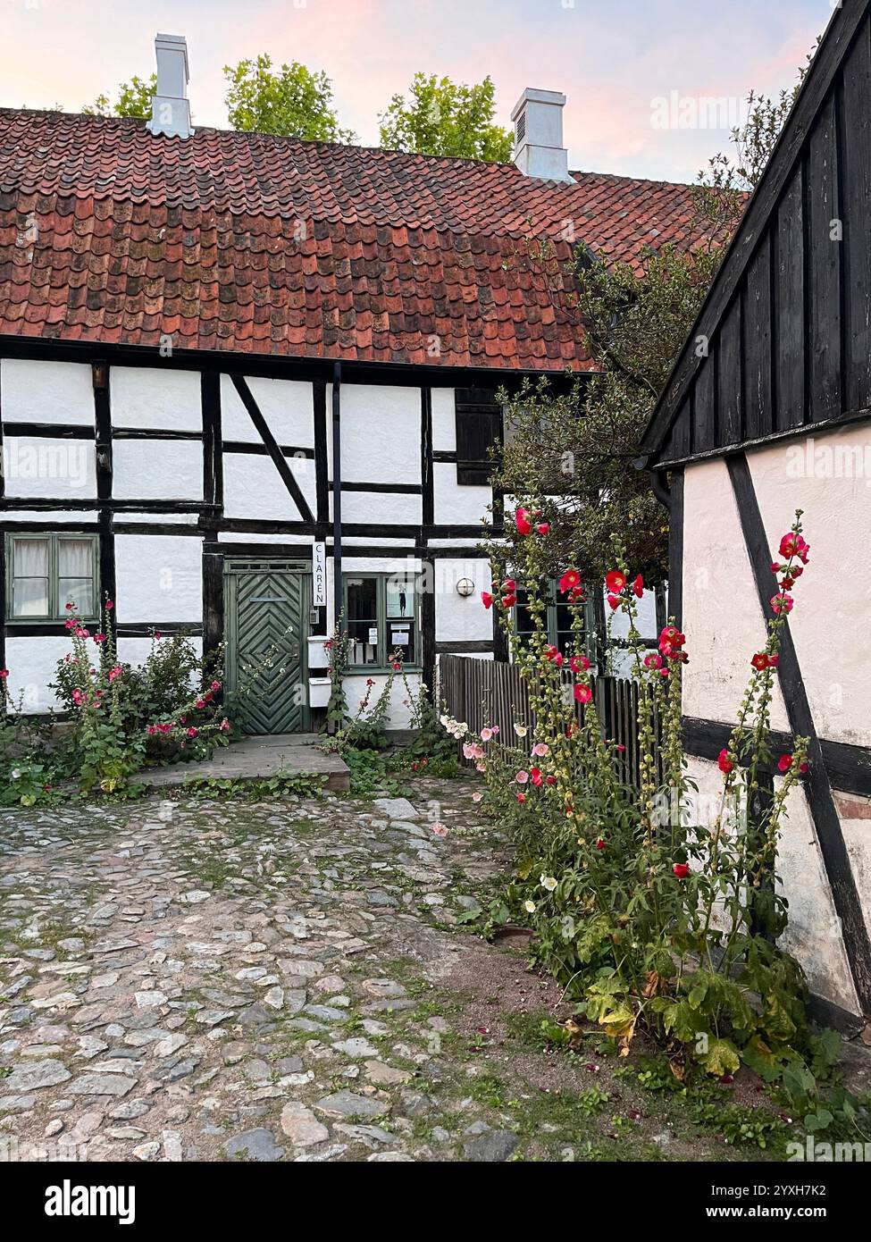 Vecchia casa bianca e marrone con porta verde e tetto in mattoni rossi e pietre di ciottoli nel cortile di fronte. Foto scattata a Österlen, Svezia, estate 2023 Foto Stock
