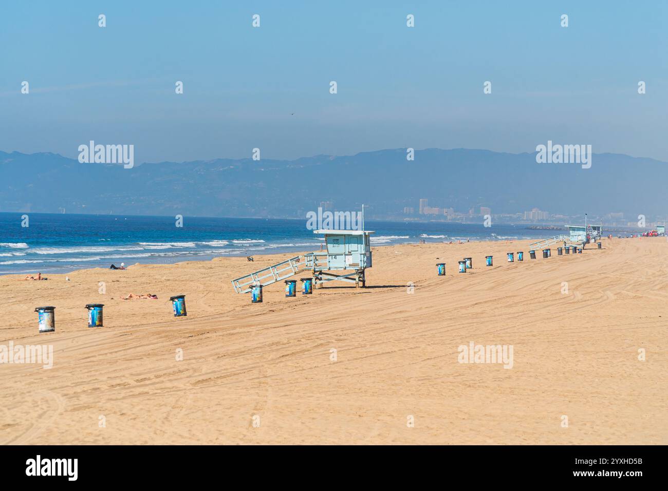 Spiaggia californiana vicino a Los Angeles con tipiche capanne bagnino, turisti che si abbronzano e bidoni della spazzatura allineati sulla sabbia Foto Stock