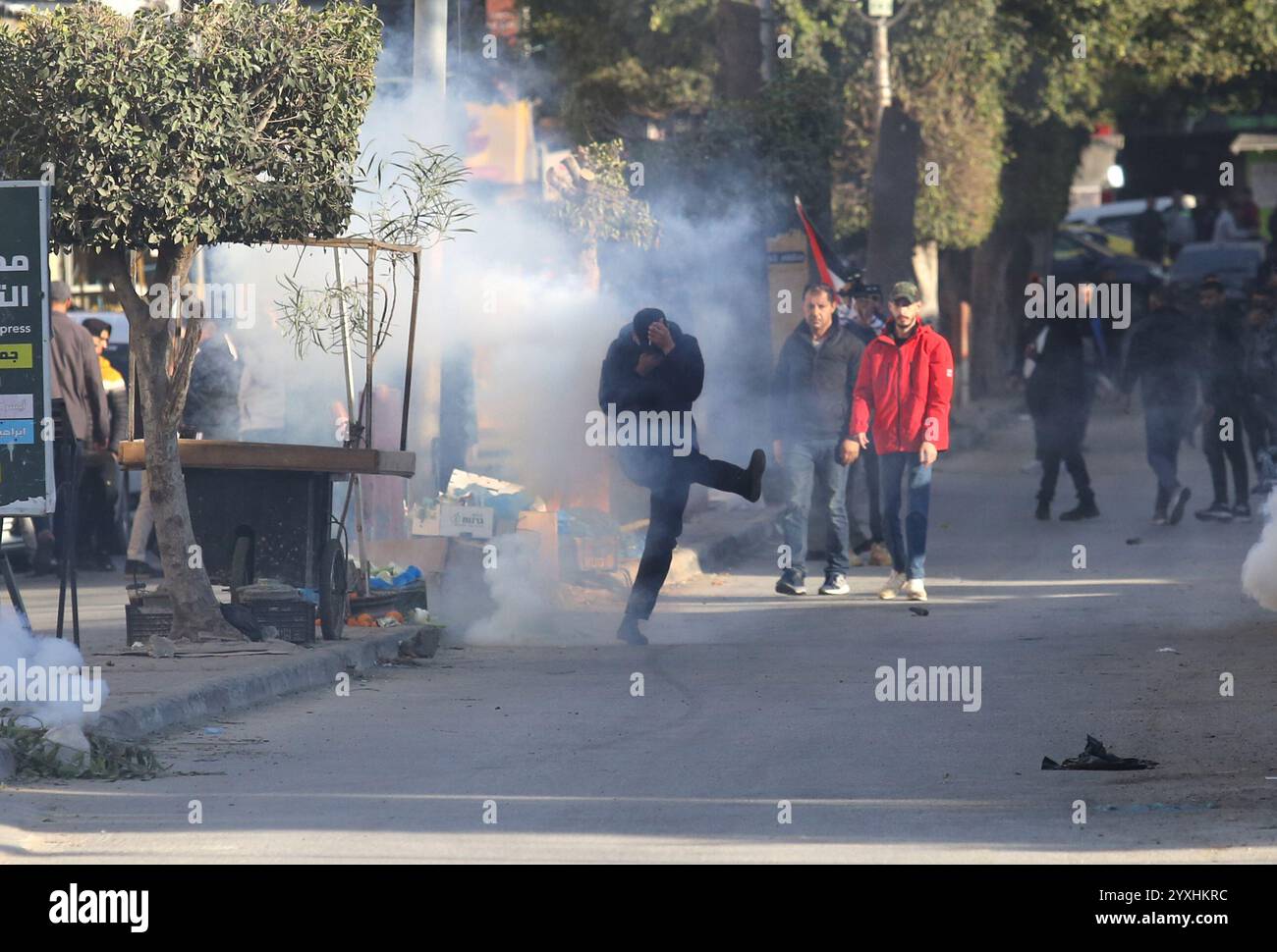 (241216) -- JENIN, 16 dicembre 2024 (Xinhua) -- Un manifestante cerca di calci una tanica di gas lacrimogeni lanciata dalle forze di sicurezza palestinesi durante una marcia che chiede la revoca dell'assedio al campo di Jenin, a Jenin, nella Cisgiordania settentrionale, il 16 dicembre 2024. Le forze di sicurezza palestinesi hanno assediato il campo profughi di Jenin sabato dopo che i militanti affiliati alla "Brigata Jenin” del movimento della Jihad islamica e altre fazioni palestinesi hanno sequestrato due veicoli appartenenti all'Autorità palestinese il 5 dicembre, secondo la fonte, che hanno richiesto l'anonimato. Crediti: Xinhua/Alamy Live News Foto Stock