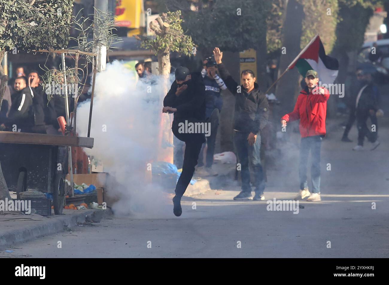 (241216) -- JENIN, 16 dicembre 2024 (Xinhua) -- Un manifestante cerca di calci una tanica di gas lacrimogeni lanciata dalle forze di sicurezza palestinesi durante una marcia che chiede la revoca dell'assedio al campo di Jenin, a Jenin, nella Cisgiordania settentrionale, il 16 dicembre 2024. Le forze di sicurezza palestinesi hanno assediato il campo profughi di Jenin sabato dopo che i militanti affiliati alla "Brigata Jenin” del movimento della Jihad islamica e altre fazioni palestinesi hanno sequestrato due veicoli appartenenti all'Autorità palestinese il 5 dicembre, secondo la fonte, che hanno richiesto l'anonimato. Crediti: Xinhua/Alamy Live News Foto Stock