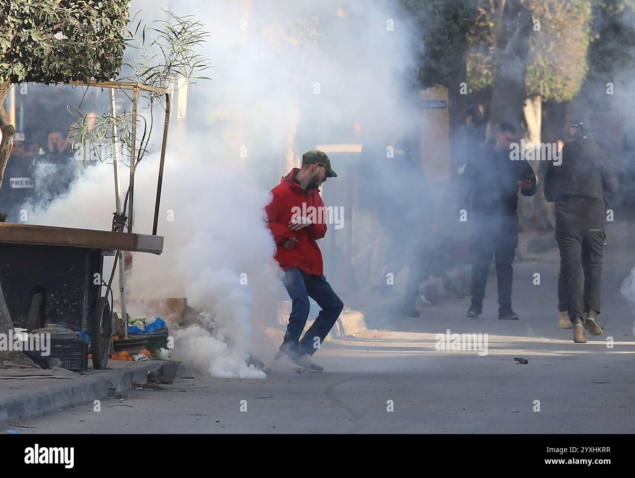 (241216) -- JENIN, 16 dicembre 2024 (Xinhua) -- Un manifestante cerca di coprire i contenitori di gas lacrimogeni lanciati dalle forze di sicurezza palestinesi durante una marcia che chiede la revoca dell'assedio al campo di Jenin, a Jenin, nella Cisgiordania settentrionale, il 16 dicembre 2024. Le forze di sicurezza palestinesi hanno assediato il campo profughi di Jenin sabato dopo che i militanti affiliati alla "Brigata Jenin” del movimento della Jihad islamica e altre fazioni palestinesi hanno sequestrato due veicoli appartenenti all'Autorità palestinese il 5 dicembre, secondo la fonte, che hanno richiesto l'anonimato. Crediti: Xinhua/Alamy Live News Foto Stock