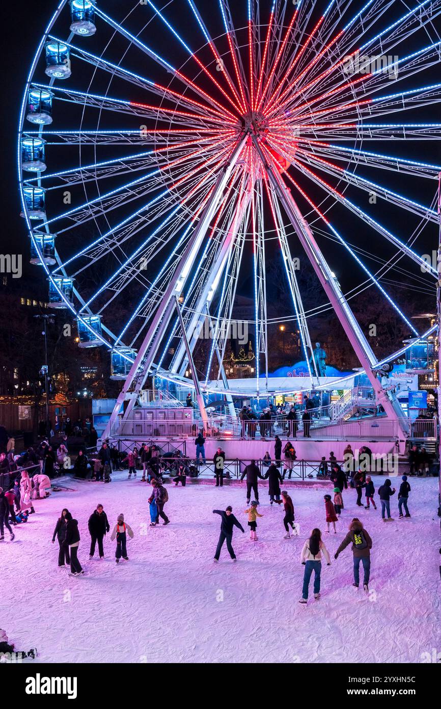 Persone che pattinano su una pista di pattinaggio al mercato di Natale di Oslo con la ruota panoramica illuminata che si illumina sullo sfondo durante la notte Foto Stock