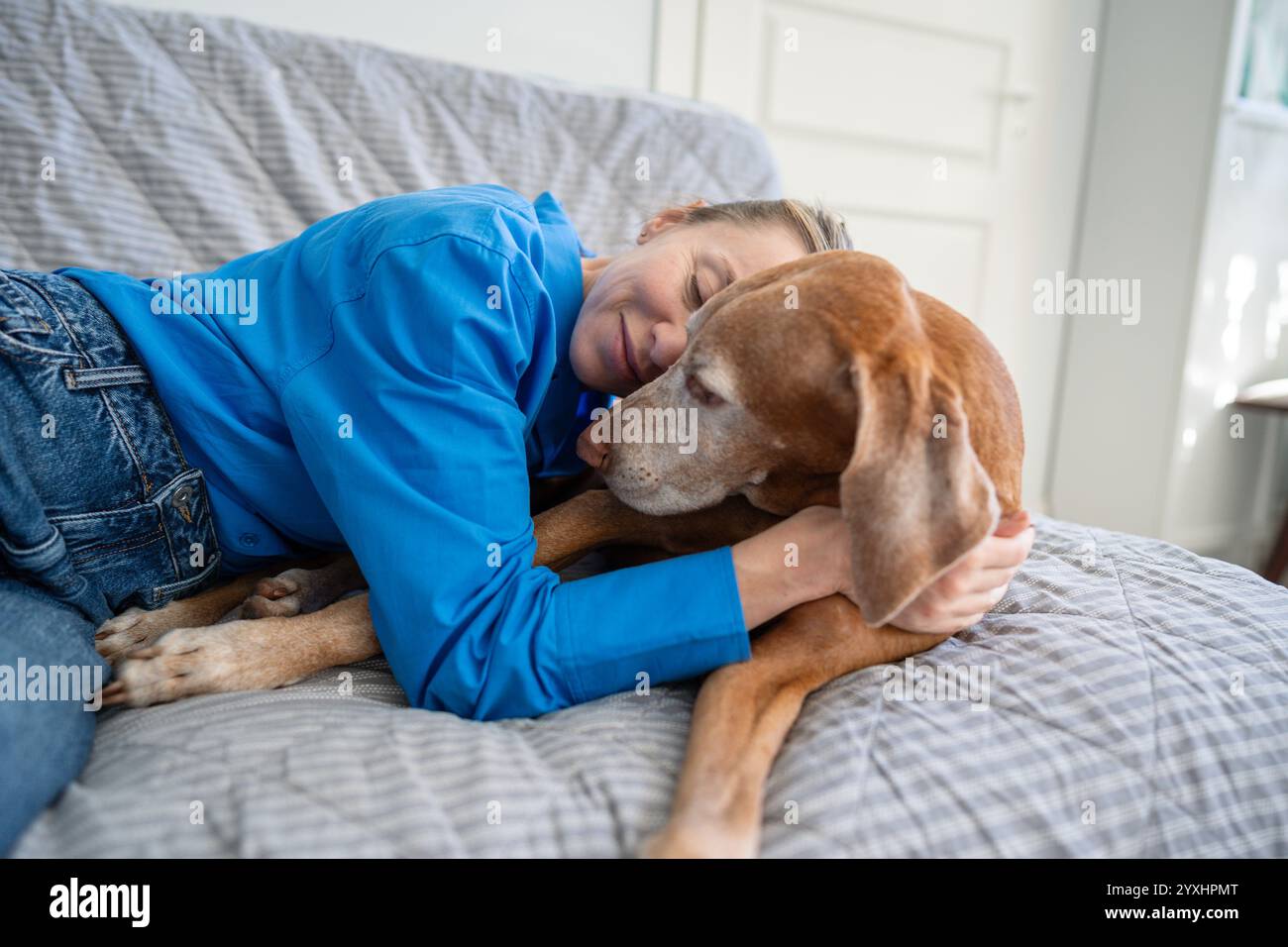 Amore incondizionato per il cane. Una donna rilassata abbraccia dolcemente il cane sul divano. Adozione animale per donna solitaria Foto Stock