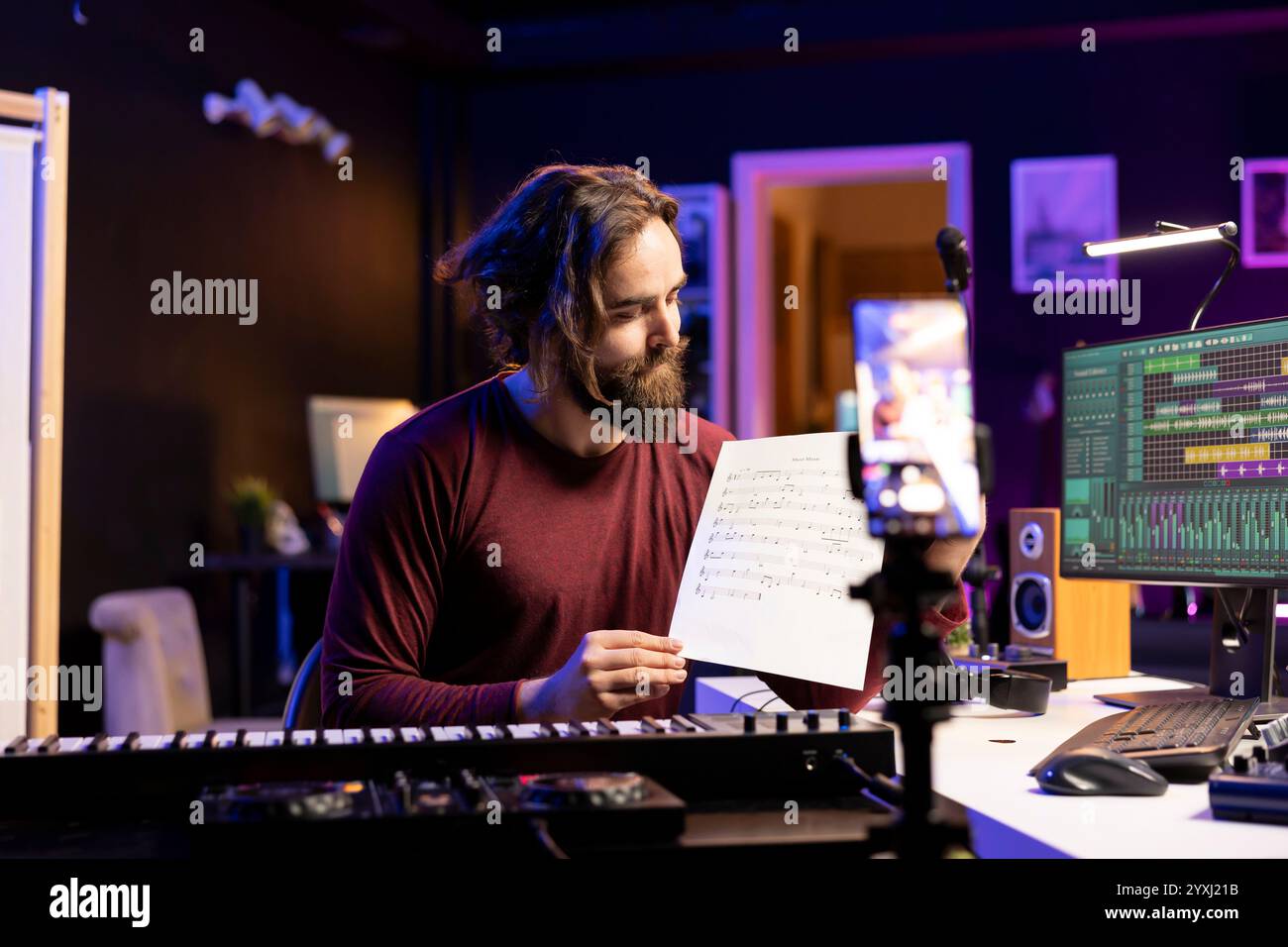 Giovane cantante che punta allo spartito musicale per spiegare le note sul sintetizzatore, insegnando alle persone come suonare il pianoforte la tastiera elettronica in casa studio. Artista che gioca ai tasti del controller Midi, vlog online. Foto Stock