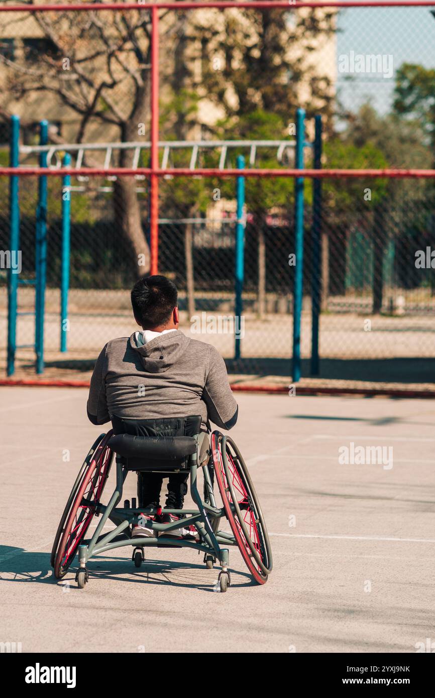 Giovane atleta latino in sedia a rotelle, allenarsi, giocare e concentrarsi con il basket in un parco cittadino all'aperto Foto Stock