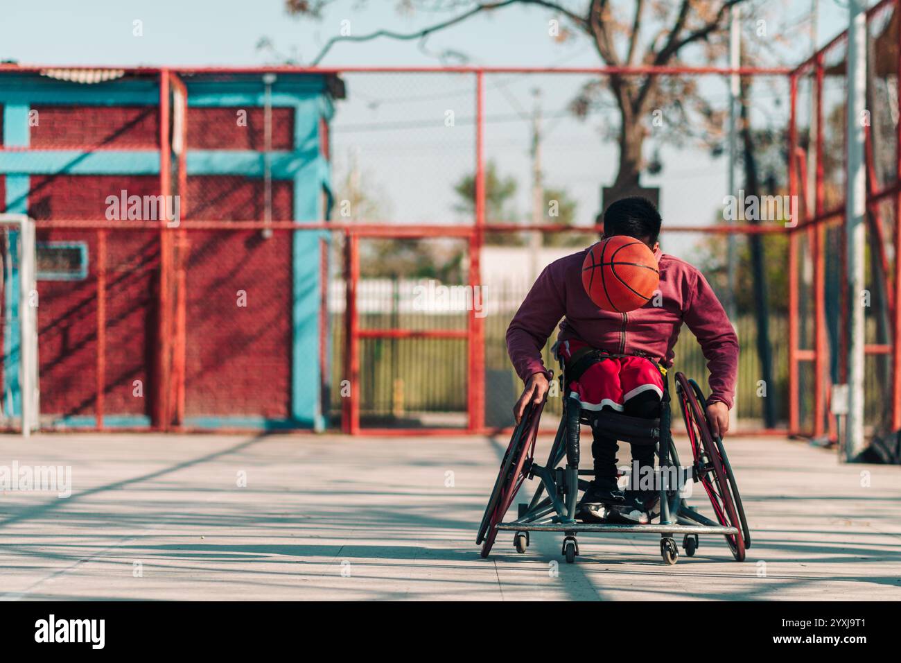 Giovane atleta latino in sedia a rotelle, allenarsi, correre, giocare e sparare la palla su un campo da basket in un parco cittadino all'aperto Foto Stock