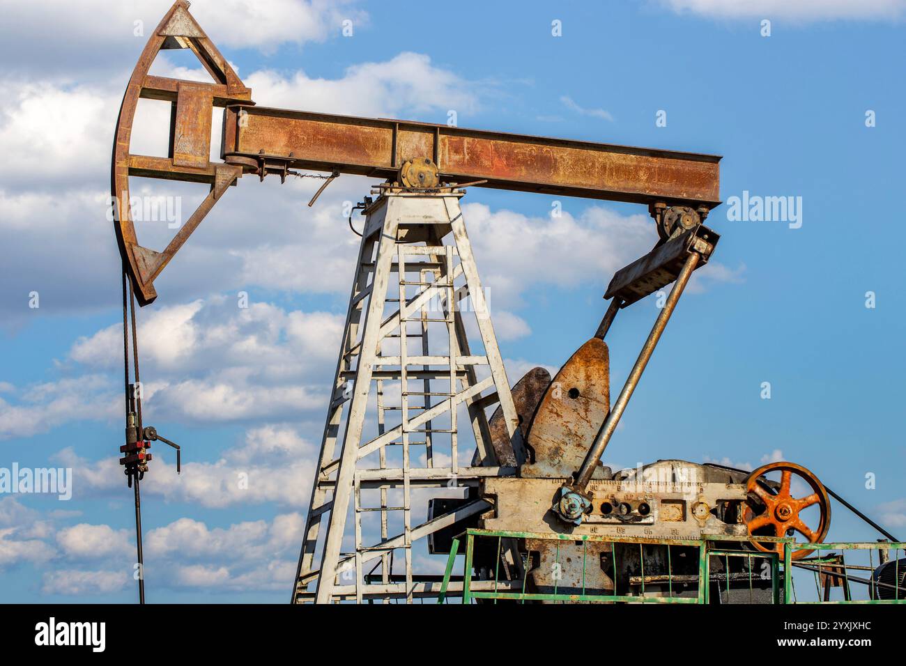 Un martinetto di pompaggio dell'olio, utilizzato per l'estrazione dell'olio, contro un cielo blu brillante con nuvole sparse. La struttura metallica è arrugginita, con ingranaggi visibili, Foto Stock