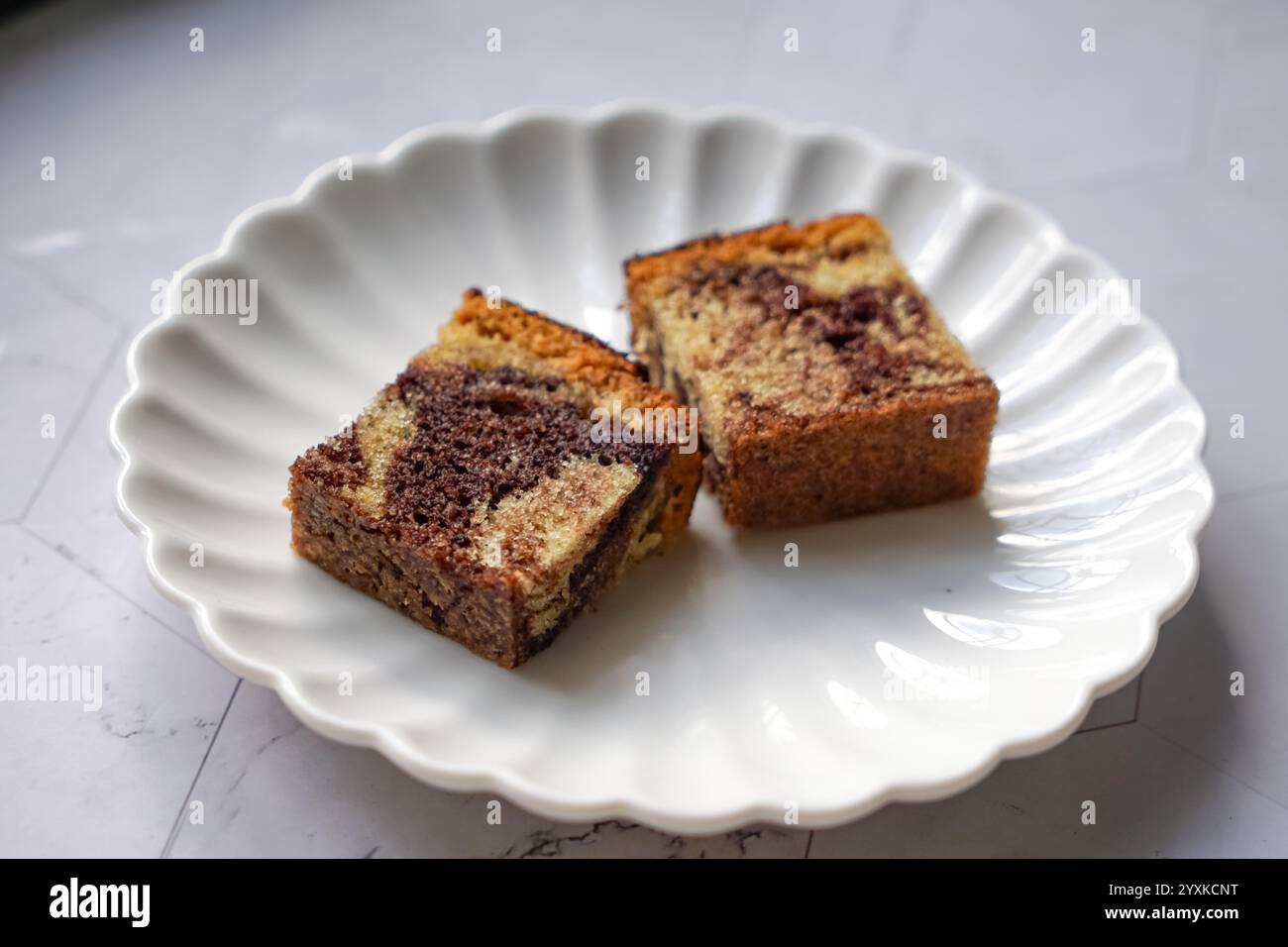 Quadrati di torta in marmo fatti in casa su un vassoio di legno con sfondo floreale per preparare il tè Foto Stock
