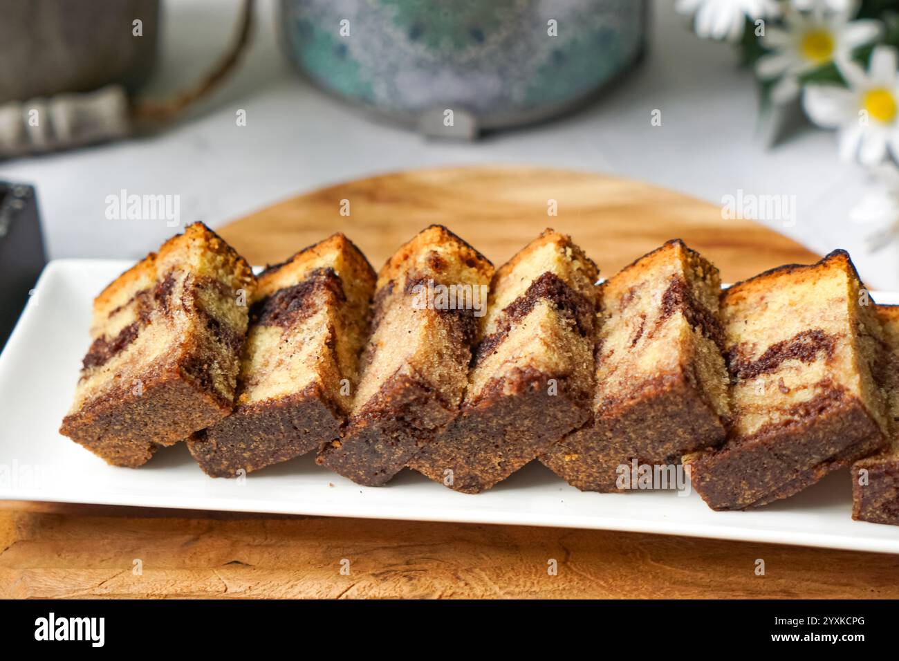 Quadrati di torta in marmo fatti in casa su un vassoio di legno con sfondo floreale per preparare il tè Foto Stock