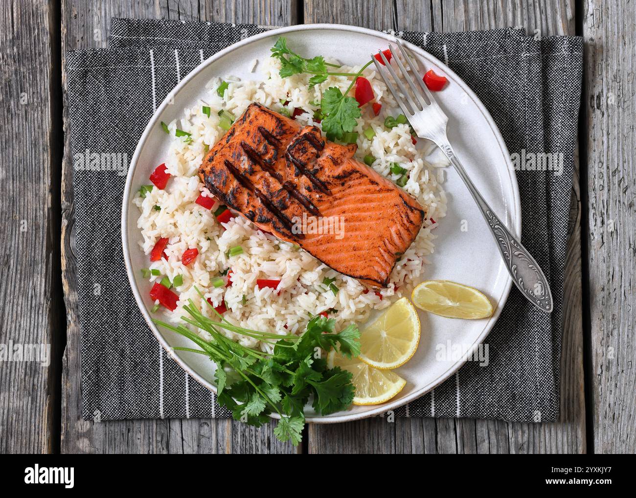 filetto di salmone rosso grigliato con riso al gelsomino, coriandolo e fette di limone sul piatto con forchetta su un tavolo in legno rustico grigio, vista orizzontale dall'alto, fla Foto Stock