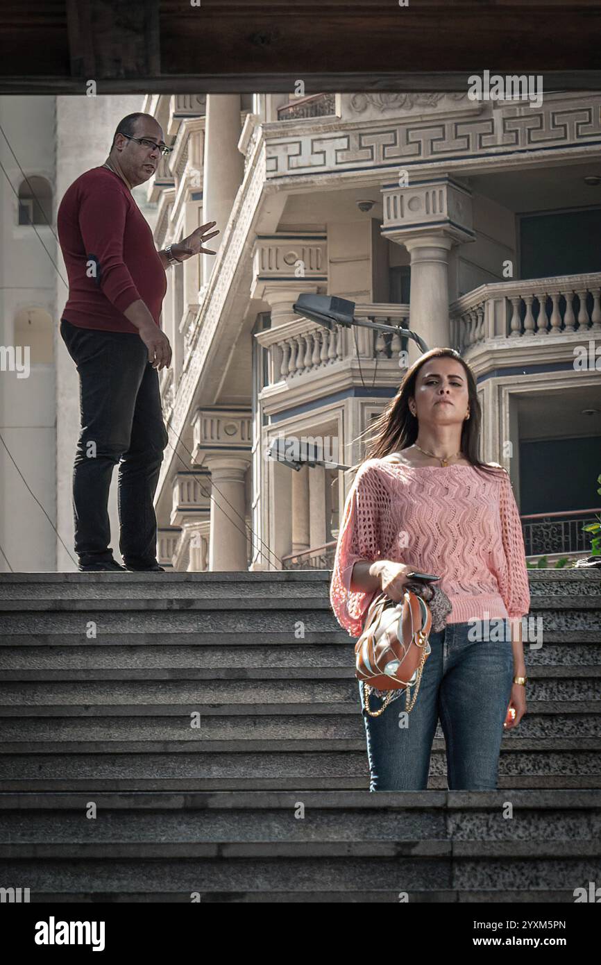 Un momento urbano teso con un uomo e una donna sulle scale di Alessandria, in Egitto, con un'architettura elegante, che evoca conflitti o molestie. Foto Stock