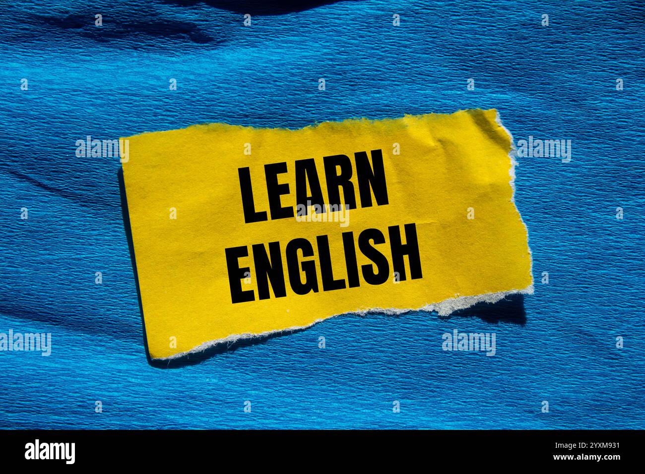 Impara il messaggio in inglese scritto su un pezzo di carta giallo strappato con sfondo blu. Simbolo Impara l'inglese concettuale. Copia spazio. Foto Stock