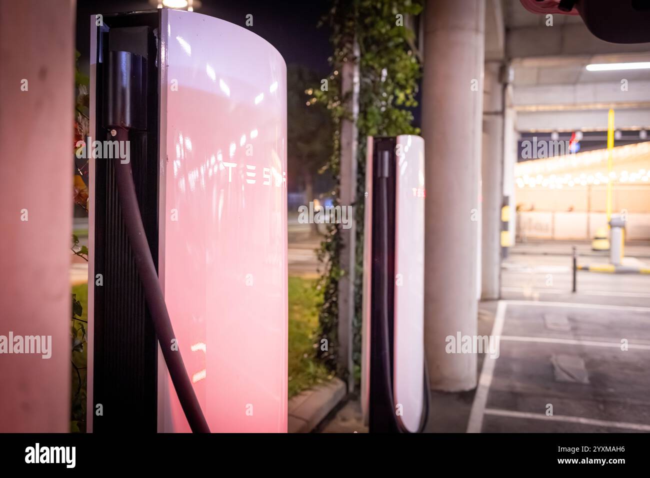 Una fila di Supercharger Tesla illuminati di notte in un ambiente urbano, con tecnologia di ricarica all'avanguardia per veicoli elettrici. Foto Stock