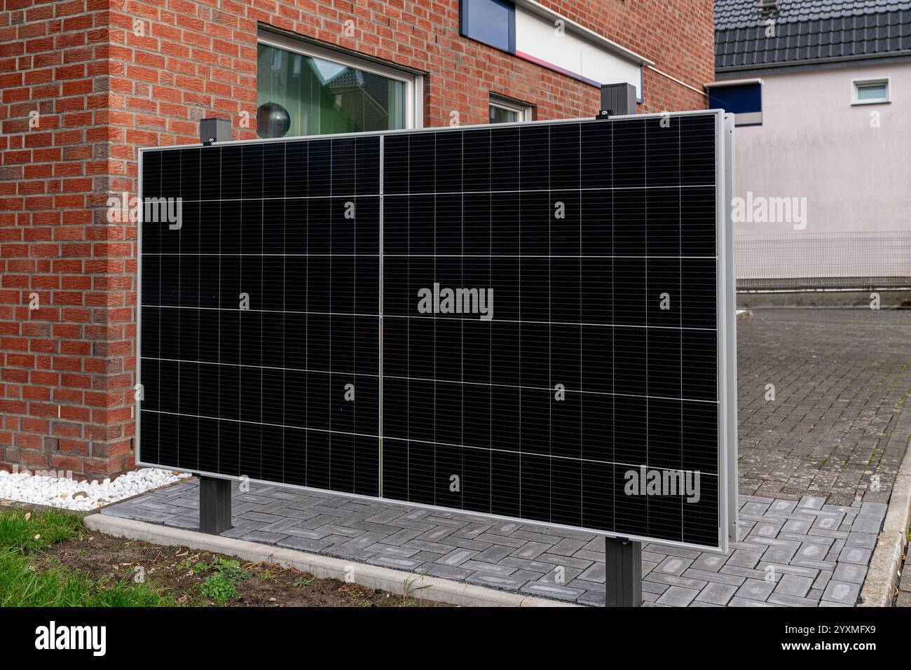 Un pannello solare è montato su un supporto vicino a un edificio in mattoni, contribuendo all'energia sostenibile in un quartiere residenziale. Foto Stock