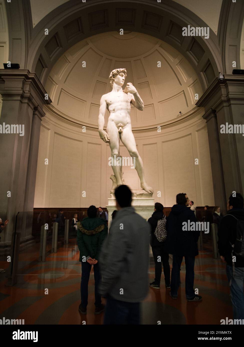 Una fotografia verticale della statua del David di Michelangelo nella Galleria dell'Accademia di Firenze, scattata il 13 dicembre 2015. I visitatori ammirano l'iconico Foto Stock