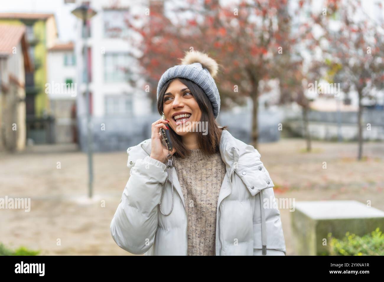 Felice e sorridente giovane donna caucasica che indossa abiti invernali che parla con il cellulare in città Foto Stock