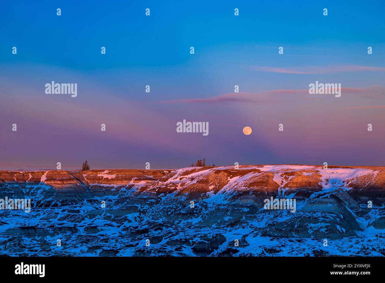 Sorge la luna d'inverno tra i raggi crepuscolari sulle calanchi dell'Horseshoe Canyon, Alberta, Canada. Foto Stock