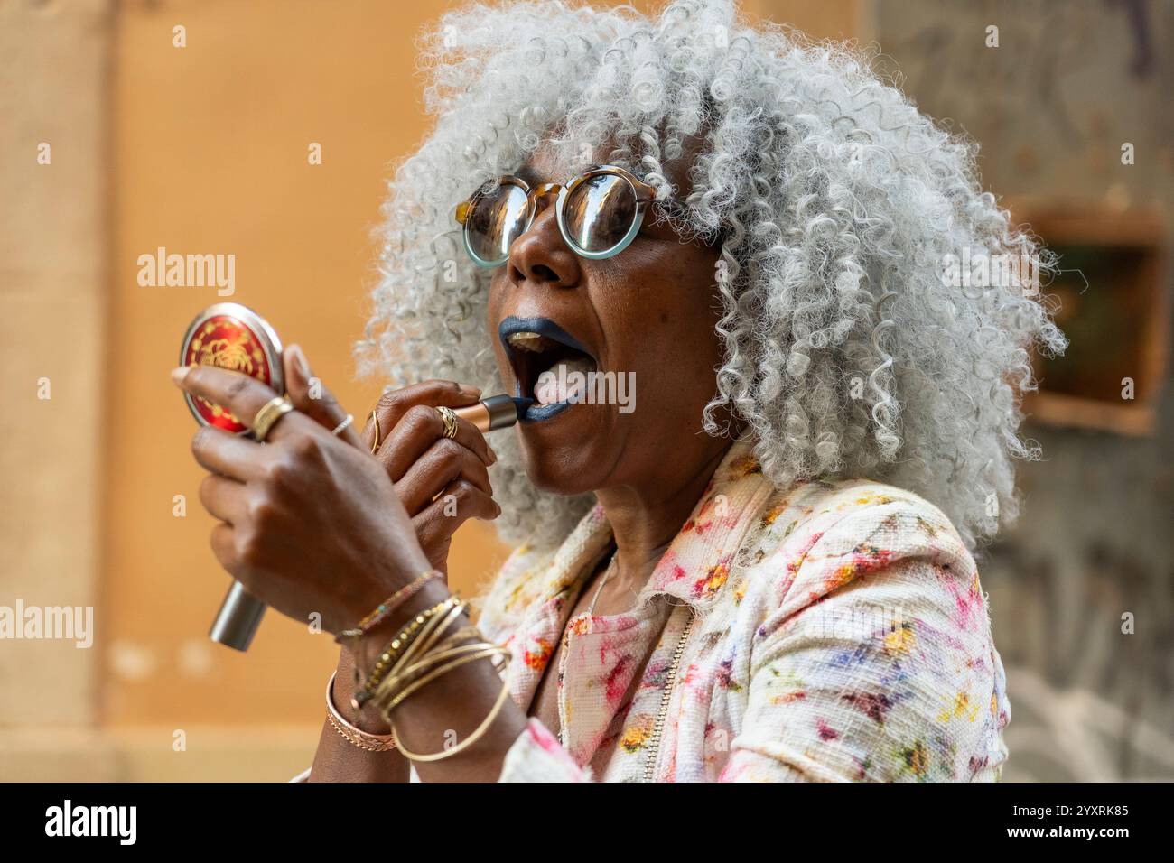 Signora nera espressiva con capelli afro e occhiali da sole che indossano rossetto blu nel soleggiato centro della città. Concetto: pro-aging, fiducia in se stessi Foto Stock