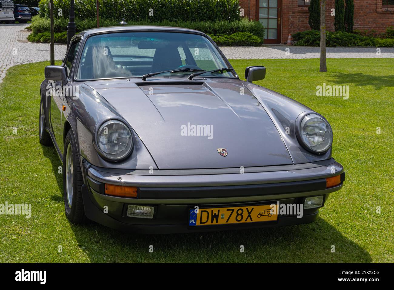 Auto sportiva d'epoca con carrozzeria grigia lucida, design classico, fari rotondi, logo Porsche e una vivace targa Foto Stock