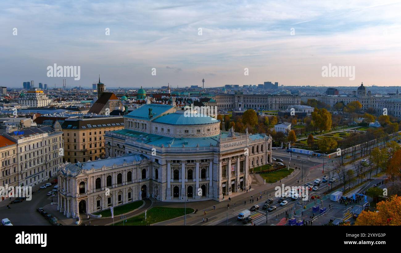 Splendida ripresa aerea dell'iconico Burgtheater di Vienna con l'architettura storica circostante, il vivace paesaggio urbano lussureggianti giardini immersi nella luce soffusa e dorata Foto Stock