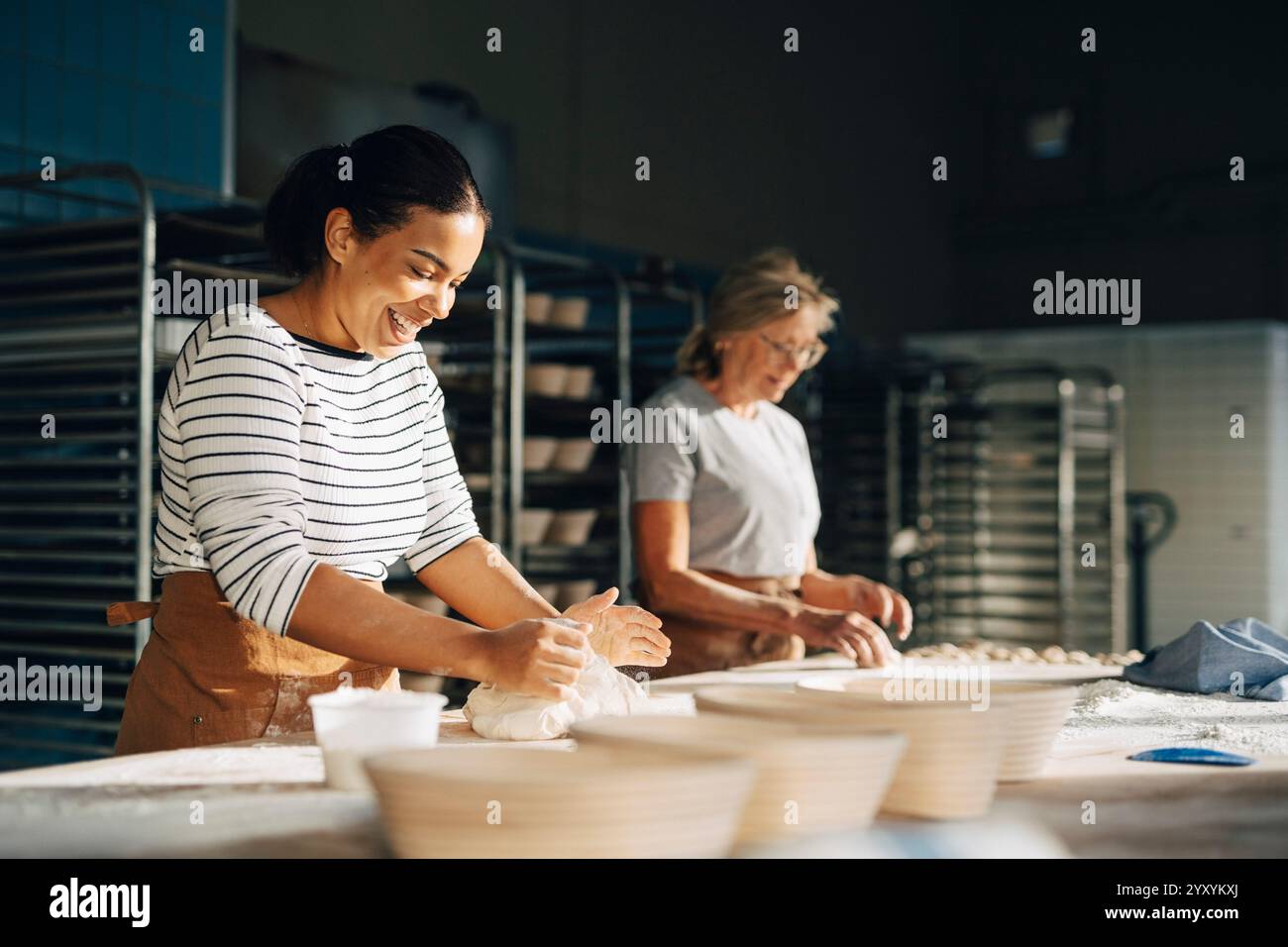 fornaio sorridente che impastava l'impasto sul tavolo mentre lavorava con la collega alla panetteria Foto Stock