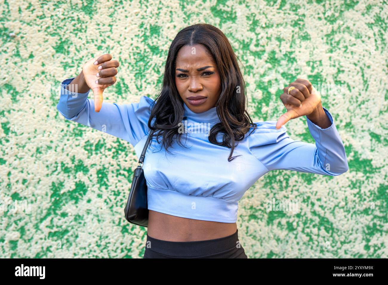 Giovane donna che mostra un gesto con i pollici che esprime disprezzo e disapprovazione in piedi su sfondo verde Foto Stock