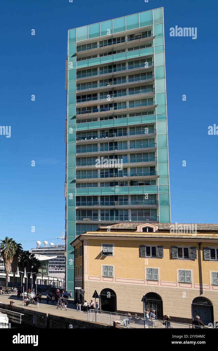 Savona, Italia - 18 dicembre 2024: Porto di Savona con un moderno e alto edificio, una nave da crociera attraccata e gente che si diverte. Contrasto delle facciate in vetro Foto Stock