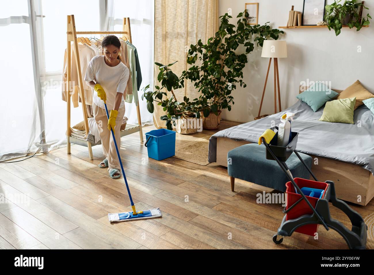 Una giovane donna afroamericana ordina la sua casa mentre pulisce il pavimento di legno nel suo appartamento. Foto Stock