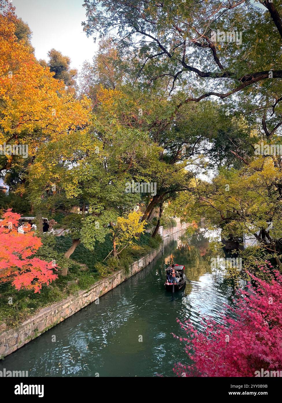 Foglie colorate di autunno sugli alberi che circondano un canale d'acqua con una piccola barca Foto Stock