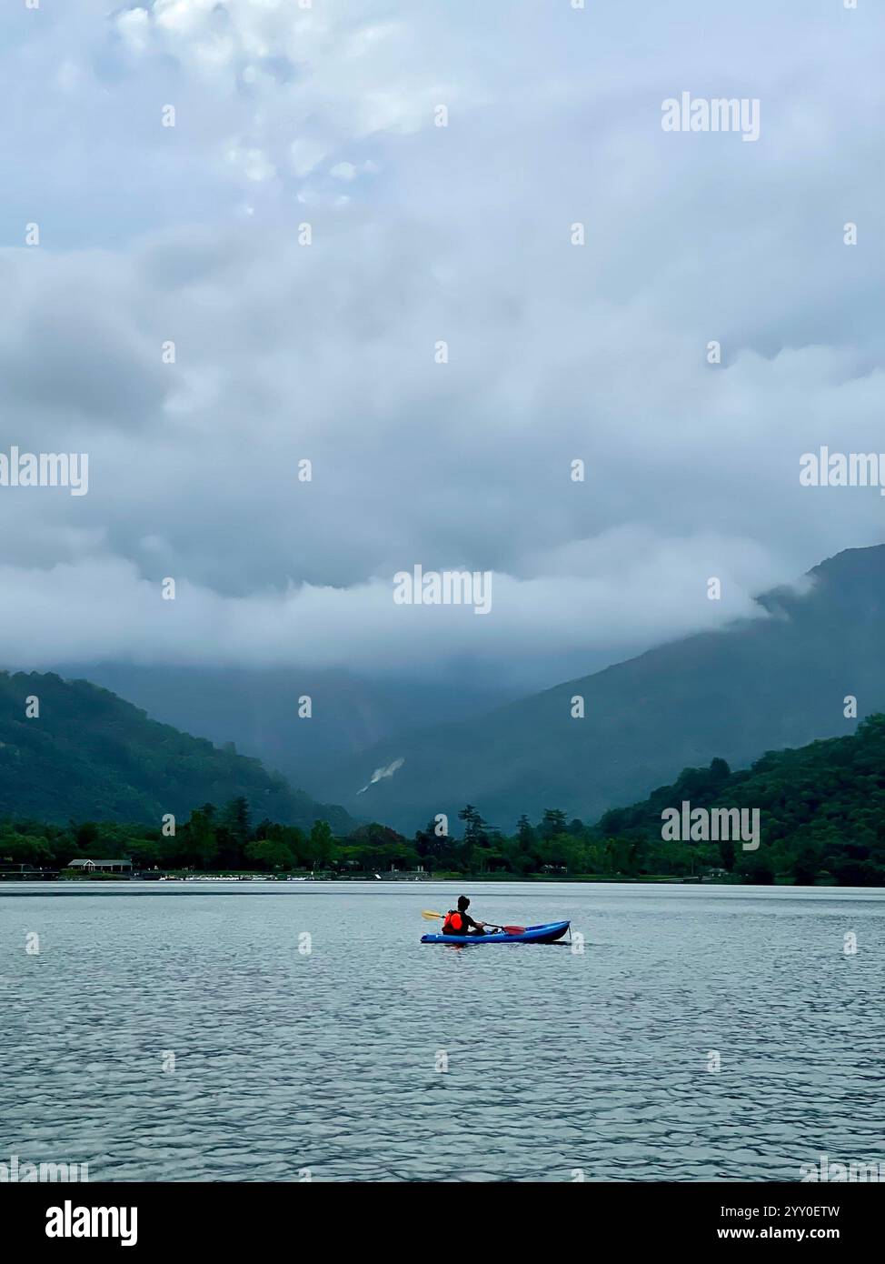 kayak singolo in un grande lago con vista sulle montagne e cielo nuvoloso - Immagine stock catturata con smartphone