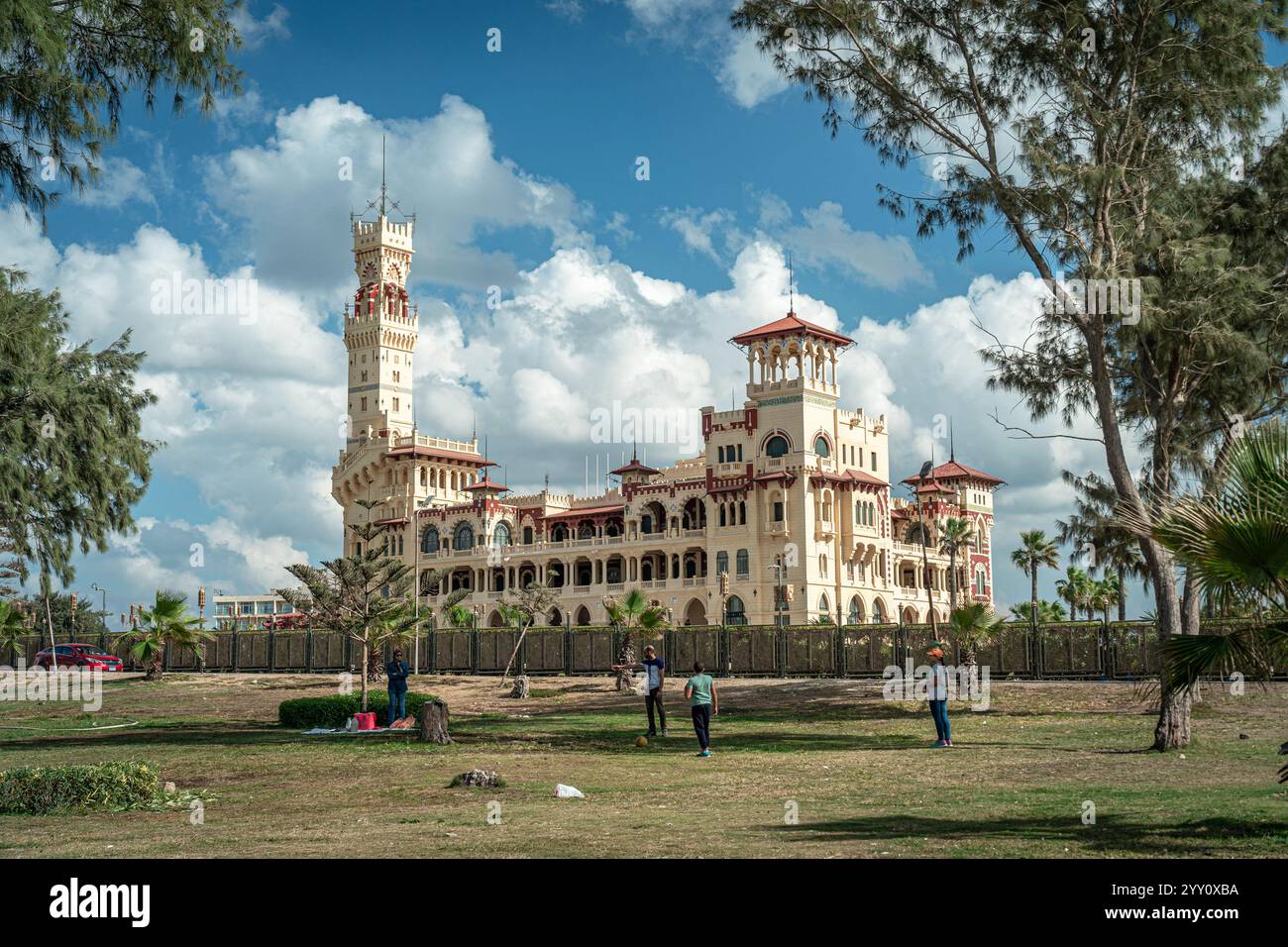 Il Palazzo di Montaza ad Alessandria, in Egitto, presenta una splendida architettura circondata da una vegetazione lussureggiante sotto un cielo vibrante, creando un paesaggio storico. Foto Stock