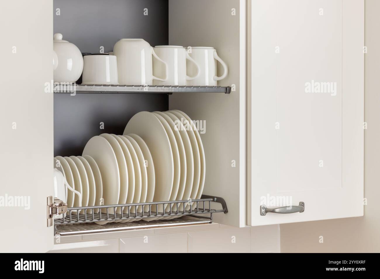 Un elegante rack in metallo per asciugare i piatti è perfettamente integrato in un armadio a parete in una cucina moderna. Il rack può contenere utensili da cucina, piatti e tazze in ceramica bianca Foto Stock