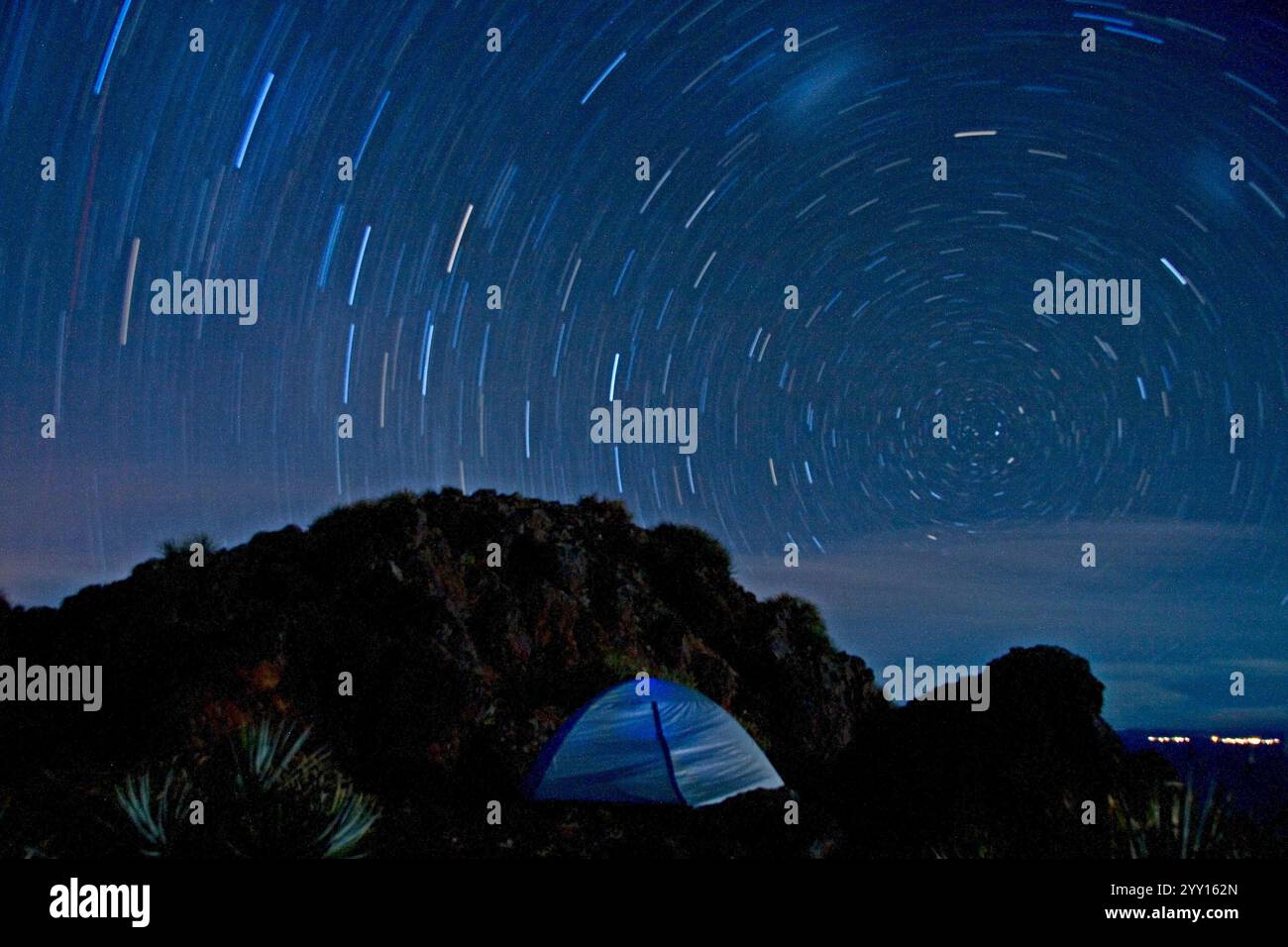 La rotazione della terra, una fotografia a lunga esposizione cattura i sentieri delle stelle formando motivi circolari nel cielo notturno sopra una tenda posizionata su un terreno roccioso. Foto Stock