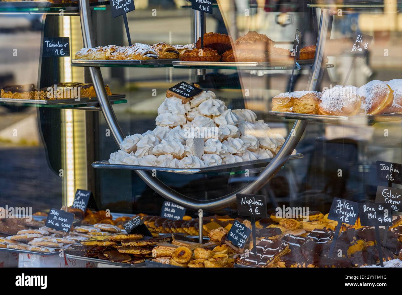 Vetrina della pasticceria con una varietà di pasticcini, meringhe e prodotti da forno, esposta ad arte con cartellini dei prezzi scritti a mano Foto Stock