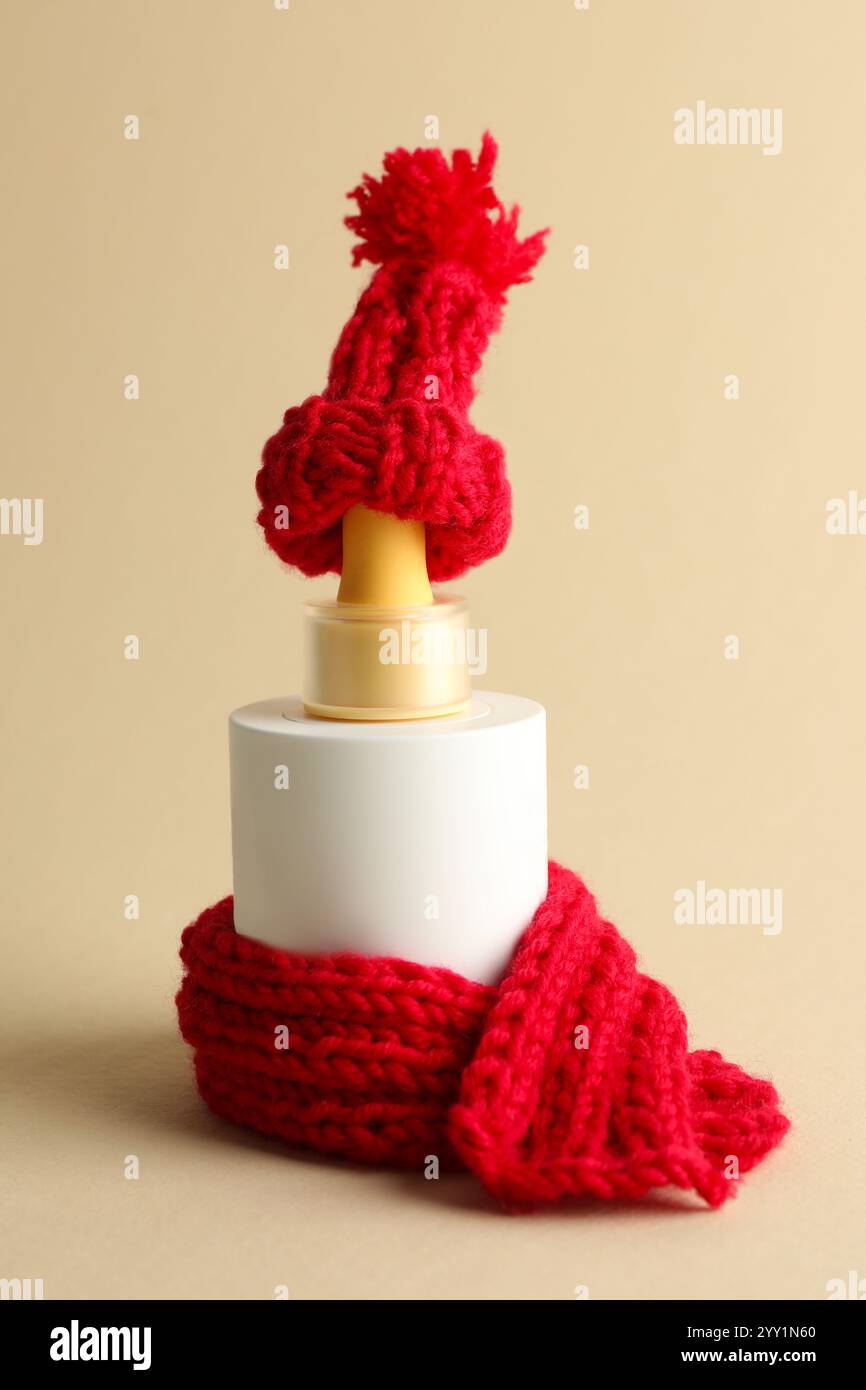 Bottiglia di prodotto per la cura della pelle con cappello rosso a maglia e sciarpa su sfondo beige Foto Stock