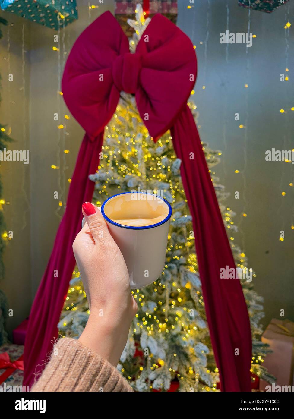 L'immagine mostra una festosa scena invernale al coperto caratterizzata da un albero di Natale splendidamente illuminato adornato da luci dorate delle fate e da una spettacolare overs Foto Stock