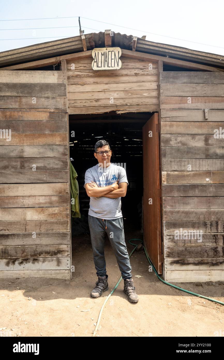 San Juan de Lurigancho, Perù – 3 settembre 2024: Il giardiniere peruviano posa con le armi attraversate dal telaio della porta "Almacen" (deposito attrezzi) Foto Stock