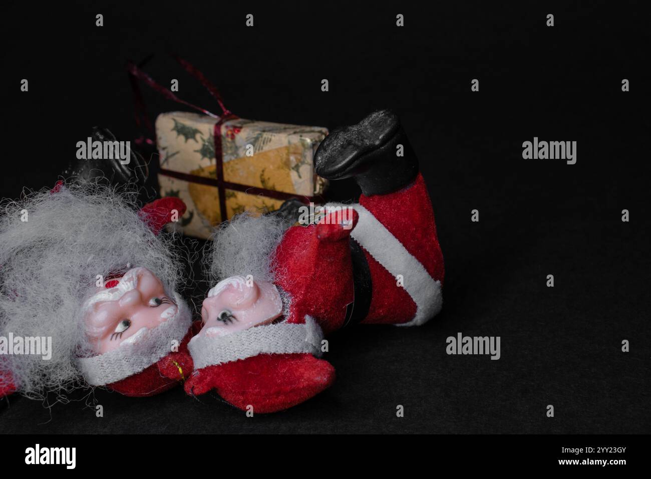Piccole figure di babbo Natale con regalo di natale adagiate sul lato sinistro di un terreno scuro, divertenti biglietti natalizi con spazio per le copie Foto Stock Piccole figure di babbo Natale con regalo di natale adagiate sul lato sinistro di un terreno scuro, divertenti biglietti natalizi con spazio per le copie Foto Stock