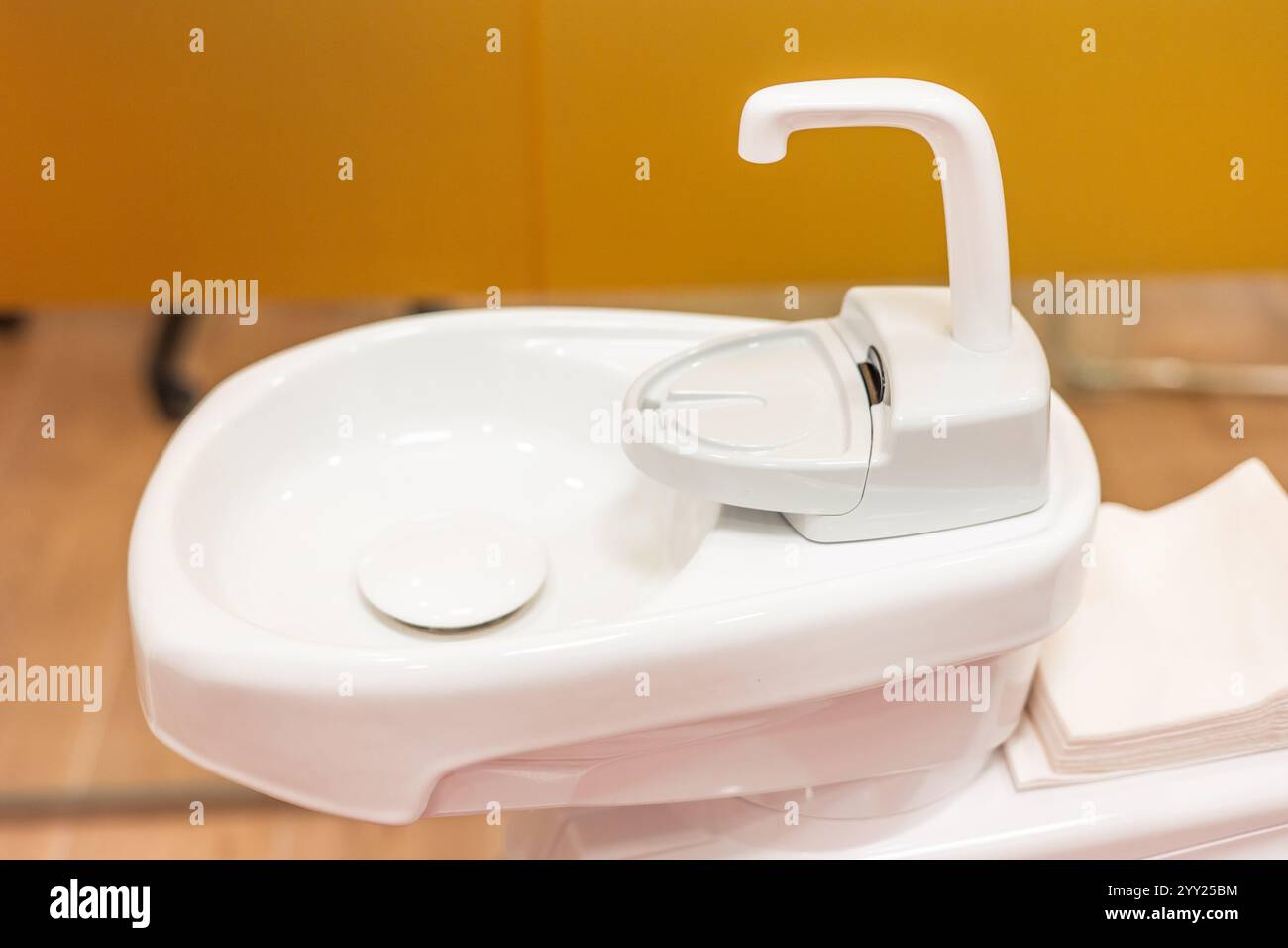 Lavabo dentista bianco, pulito e moderno con un piccolo rubinetto e portabicchieri, pronto per il risciacquo durante le procedure odontoiatriche, garantendo il comfort del paziente e l'igiene Foto Stock